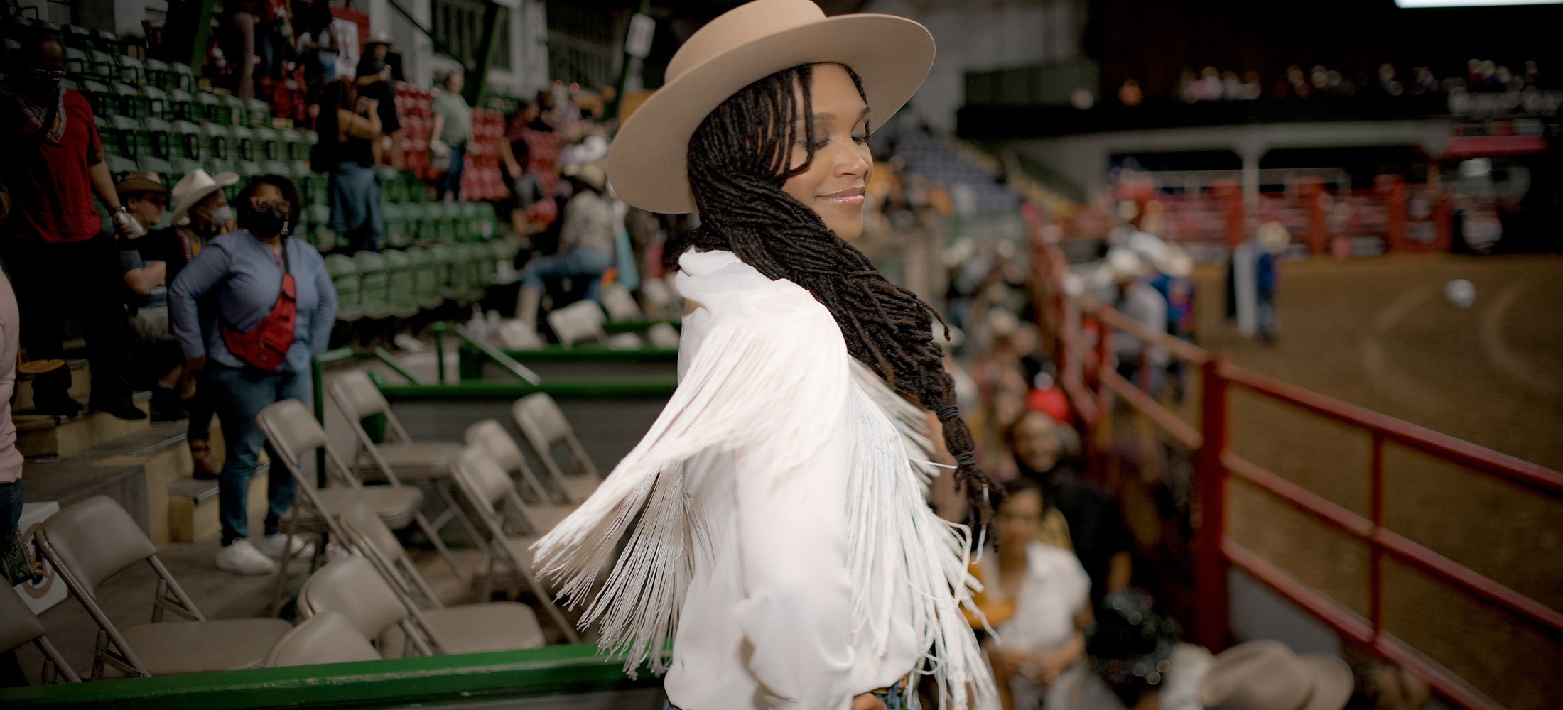 A woman wearing a white fringe jacket and twirling in a crowd of people, posing for the camera.